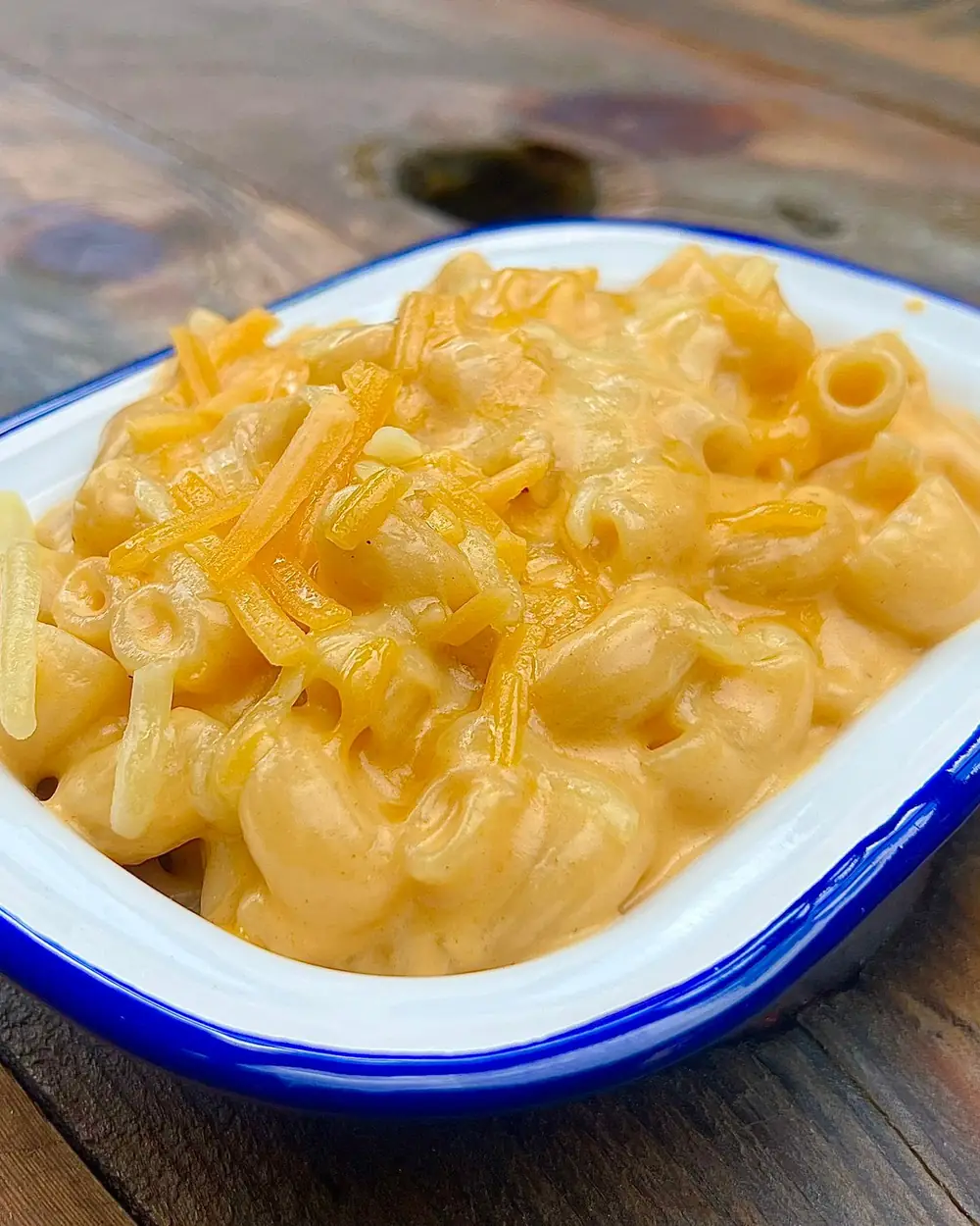 Mac and cheese topped with grated cheese in an enamel dish